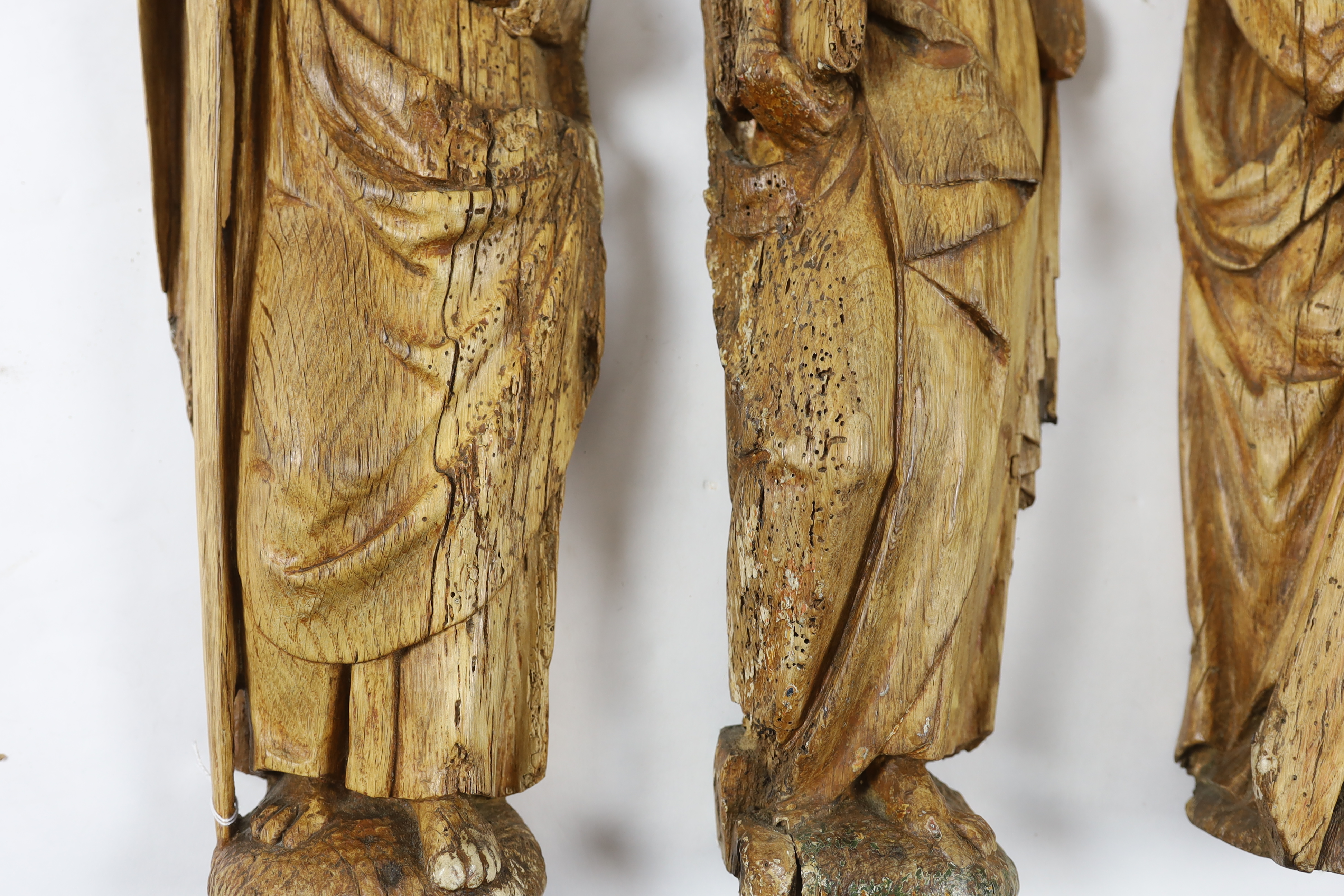 A set of three 18th century Continental carved wood figures of Saints, holding a cross, a bible and a sword, largest 17cm wide, 58cm high